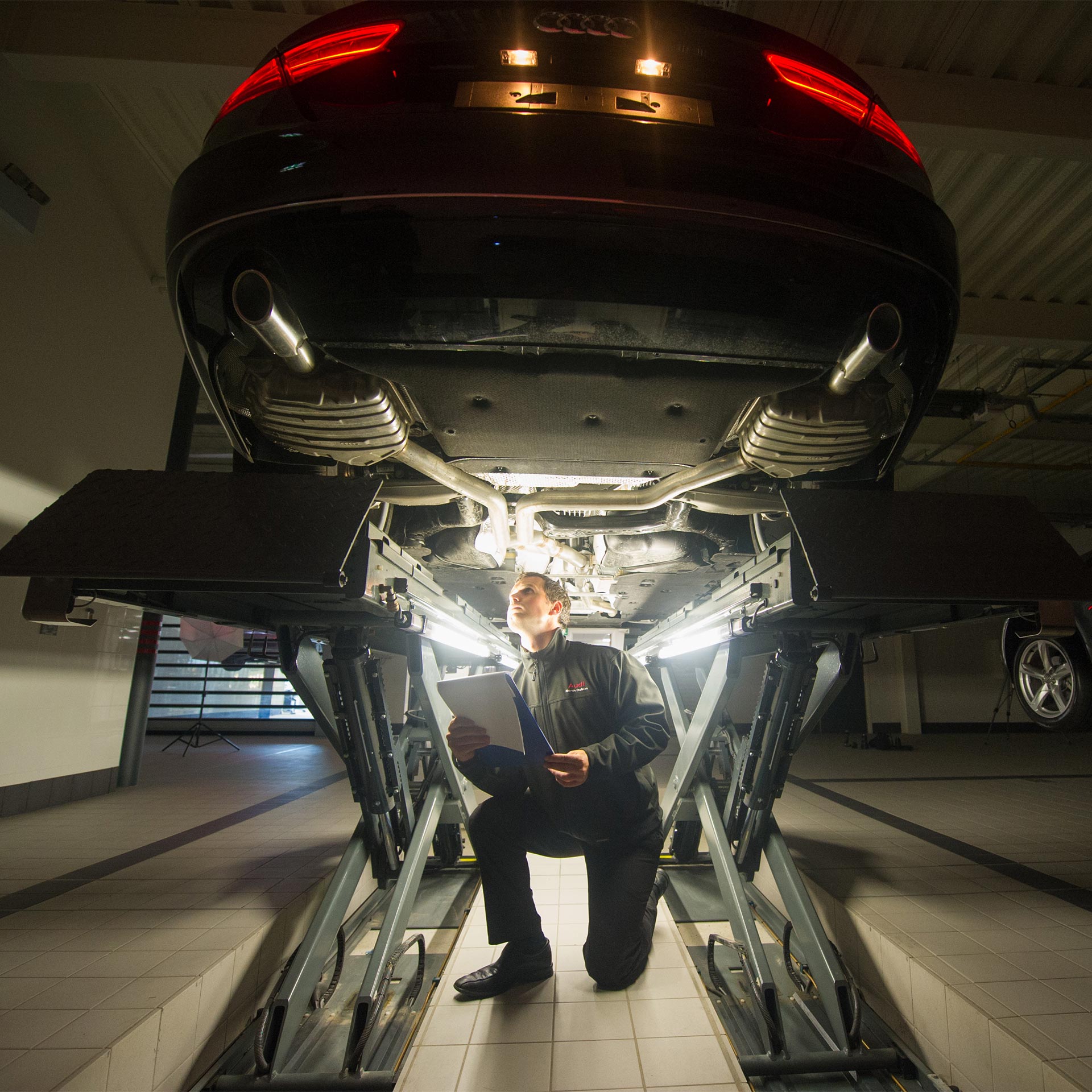 A man looking underneath an Audi that is up on a ramp at the service centre.